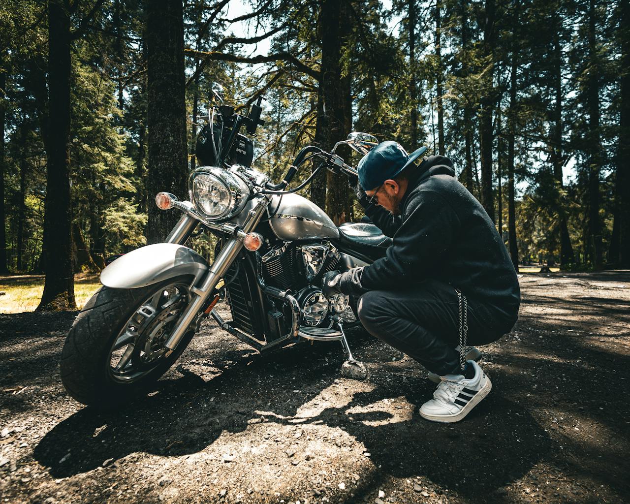 Casual man examining his motorcycle outdoors in a serene forest environment.